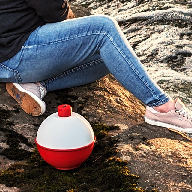 Person sitting on a rock by a flowing river with a red and white float nearby.