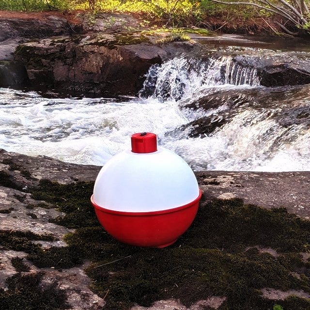 Red and white buoy on a rock with a flowing stream and waterfall in the background