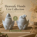 Two white urns shaped like hands holding a dog, labeled 'Heavenly Hands Urn Collection' on a wooden surface.