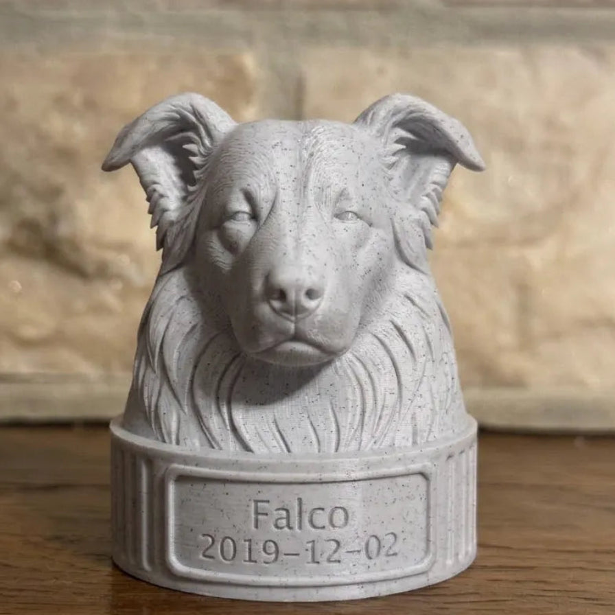 Gray stone bust of a border collie with 'Falco' and a date on a wooden surface.