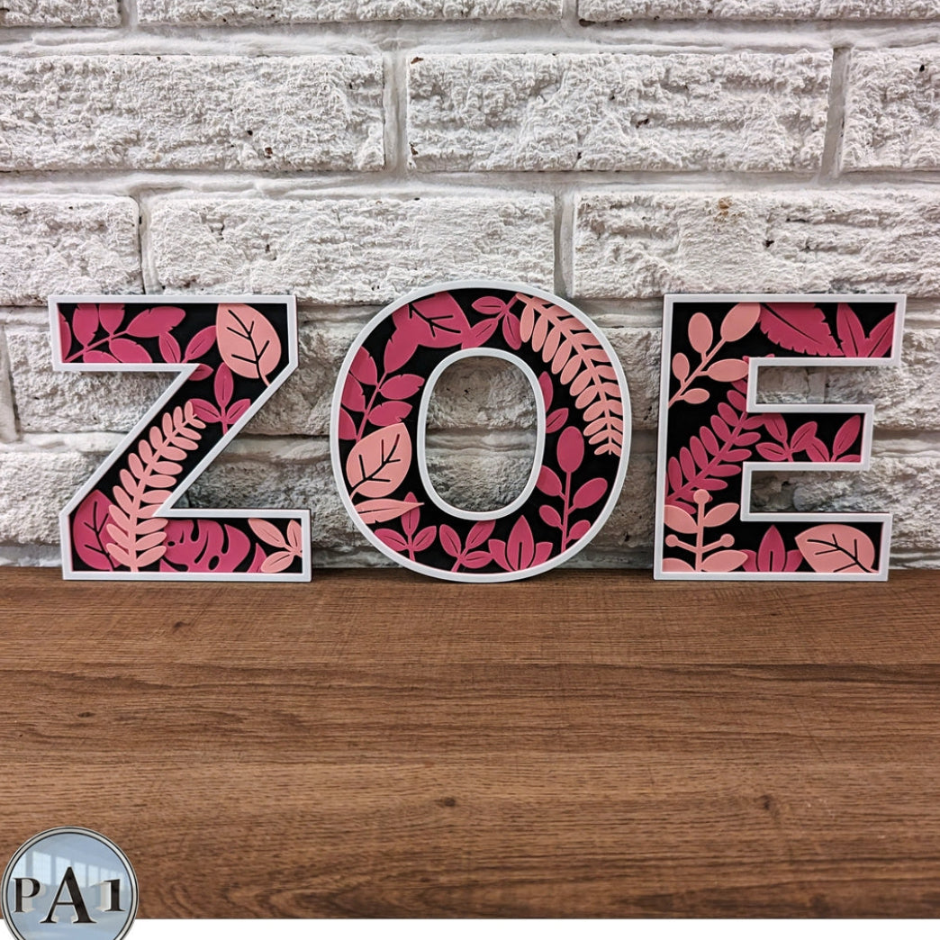 Decorative letters spelling 'ZOE' with floral patterns on a brick and wood background.