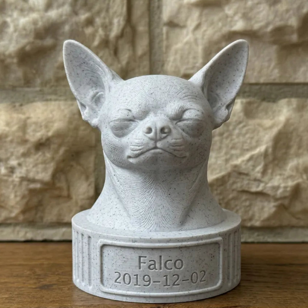 Gray stone bust of a chihuahua with 'Falco' and a date on a wooden surface against a stone wall.