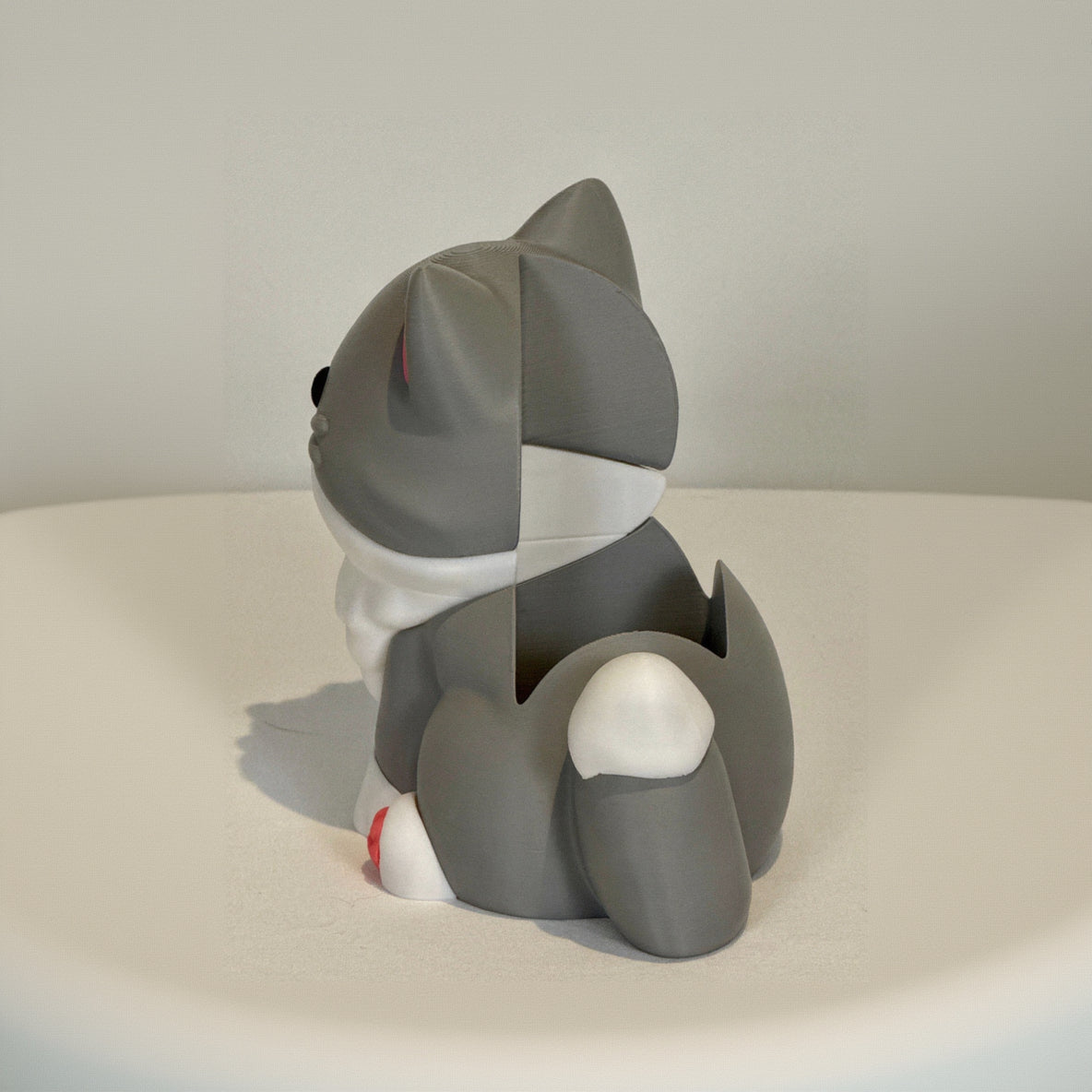 Gray and white cat-shaped object on a beige surface with a neutral background