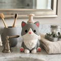 Cute gray cat-shaped soap dispenser on a bathroom counter with toothbrushes and a mirror in the background.