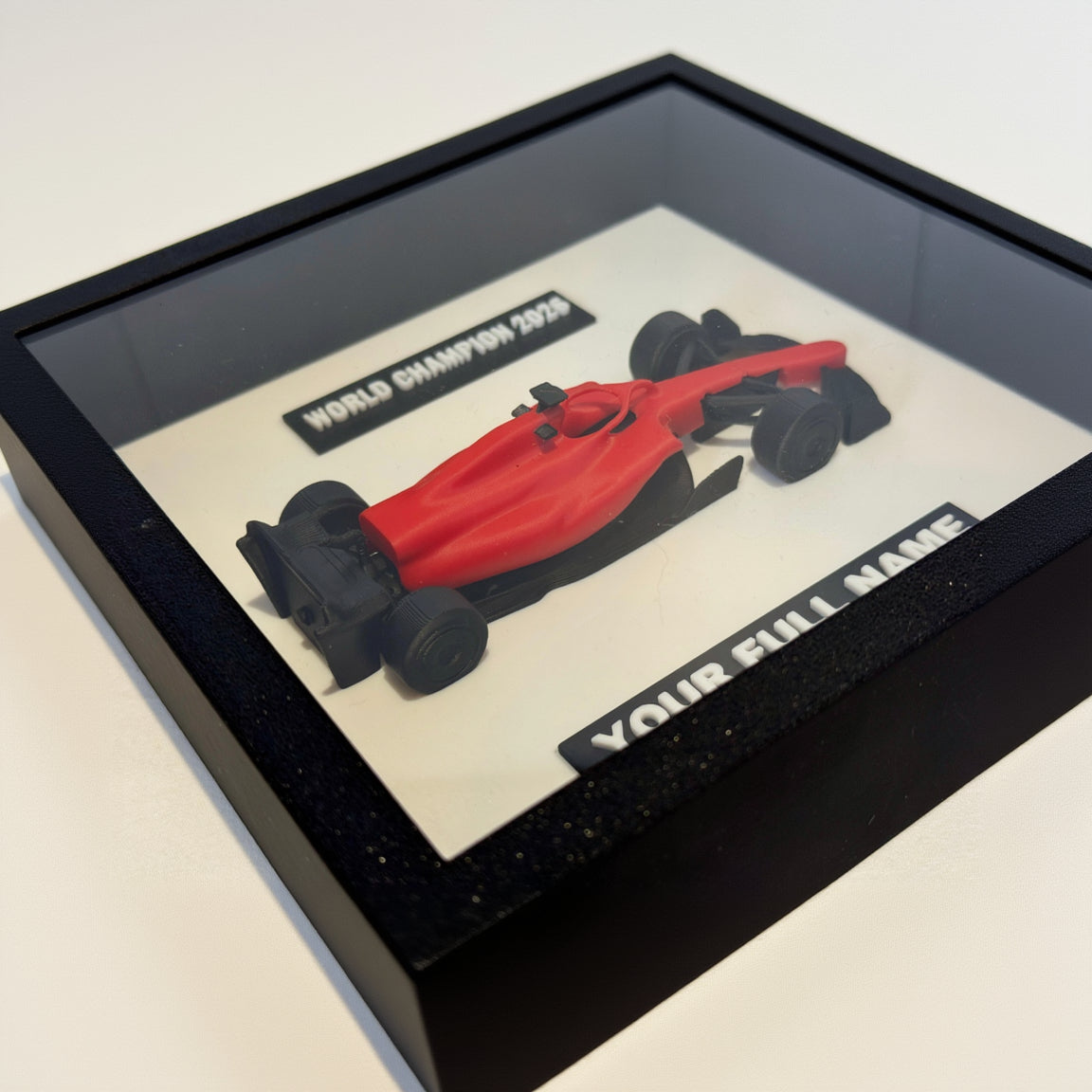 Red Formula 1 car model in a black frame with customizable text