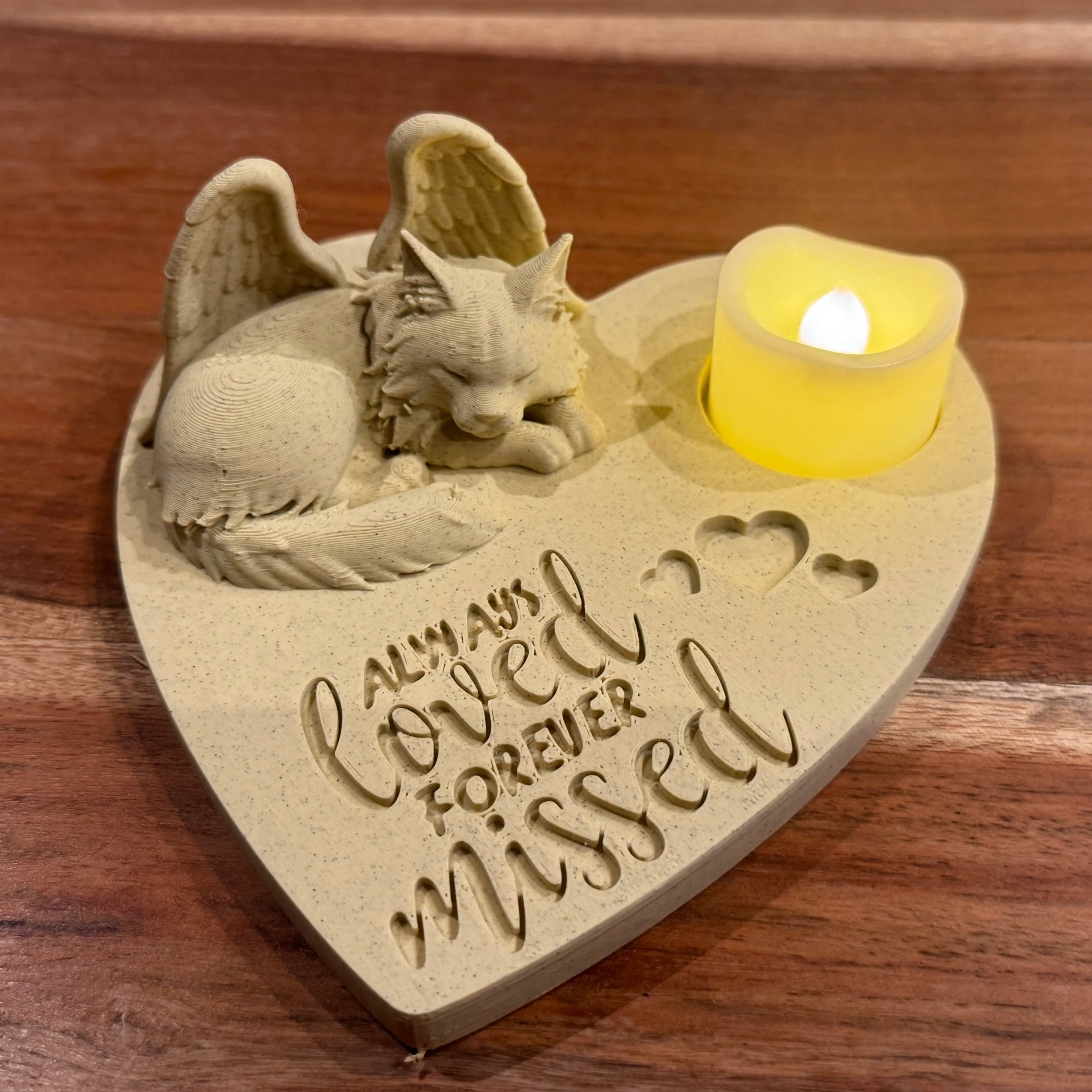Heart-shaped memorial featuring a Maine Coon cat with Angel wings figurine and candle on a wooden surface