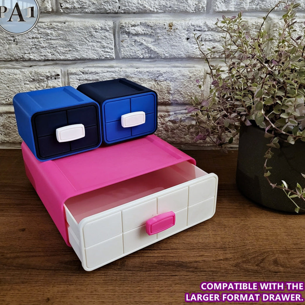 Pink and white storage box with blue and black drawers on a wooden surface with a plant in the background.
