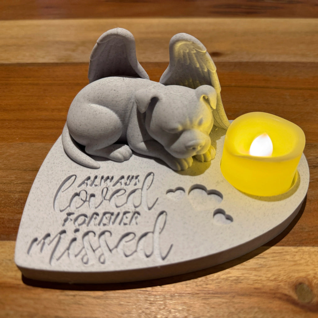 Memorial sculpture of a Pitbull with Angel wings with a candle on a wooden surface