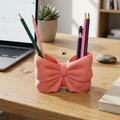 Pink bow-shaped pen holder on a desk with a laptop and books in the background