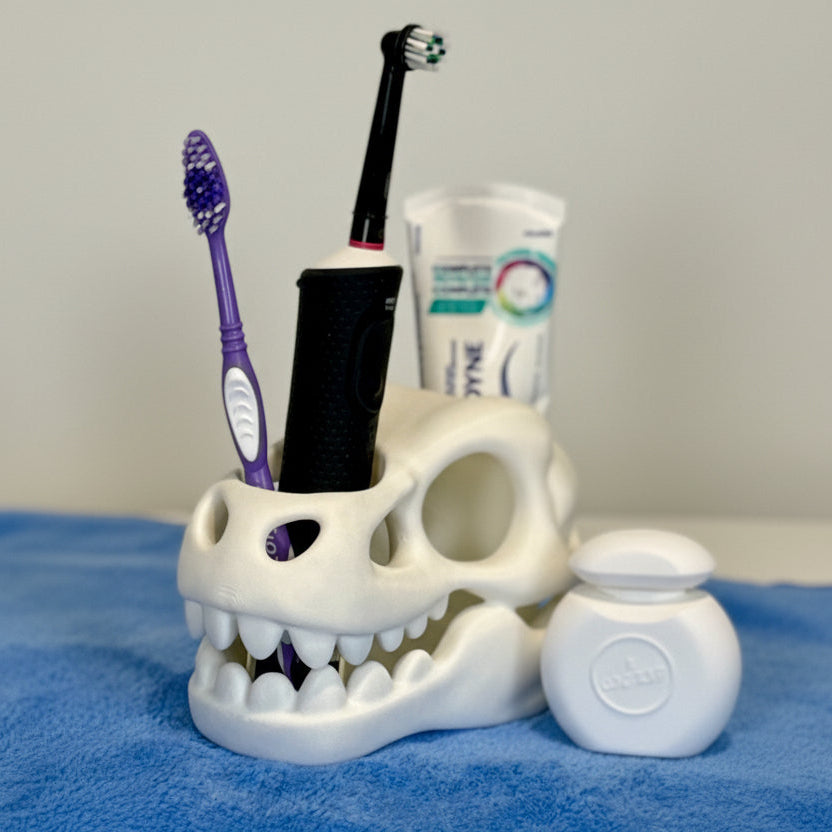 Skull-shaped toothbrush holder with toothbrushes and toothpaste on a blue surface.