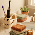Bathroom counter with skull-shaped toothbrush holder, towels, and a potted plant.