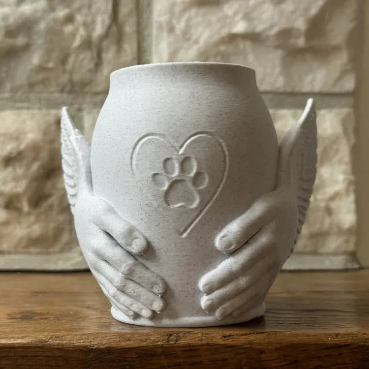 Ceramic urn with hands holding a heart and paw print design on a wooden surface.