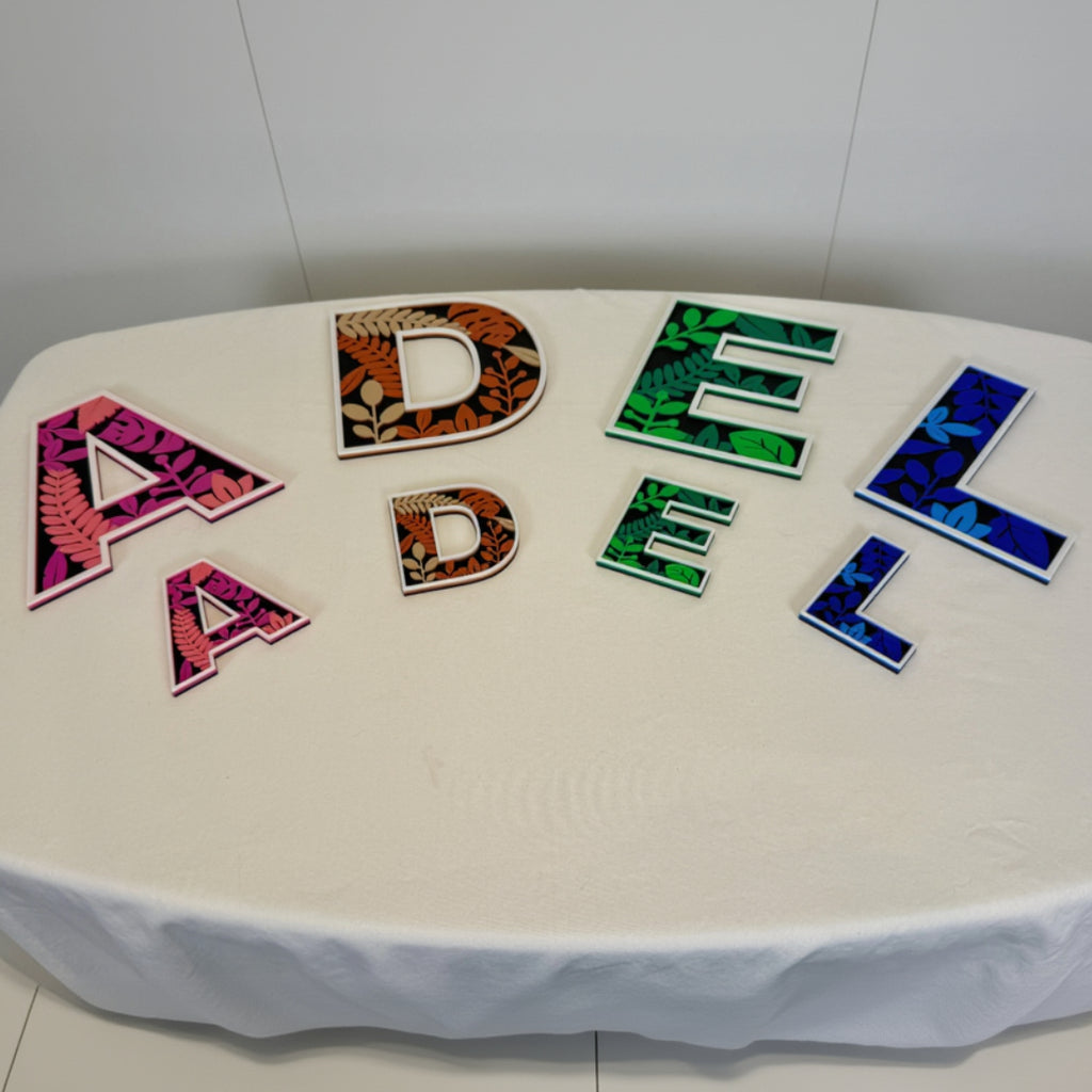 Decorative letters spelling 'ADEL' on a white surface with colorful patterns.
