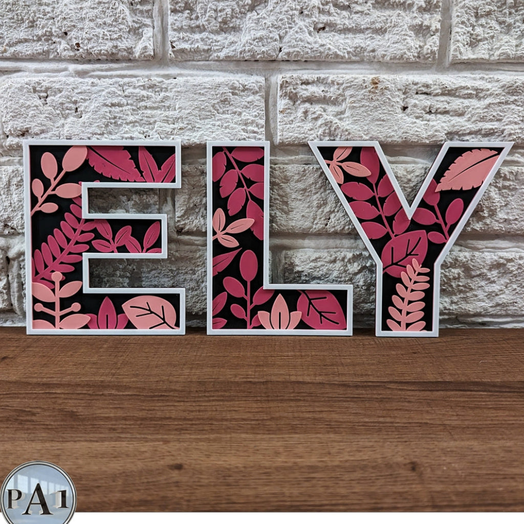 Decorative letters spelling 'ELY' with leaf pattern on a stone wall and wooden surface.