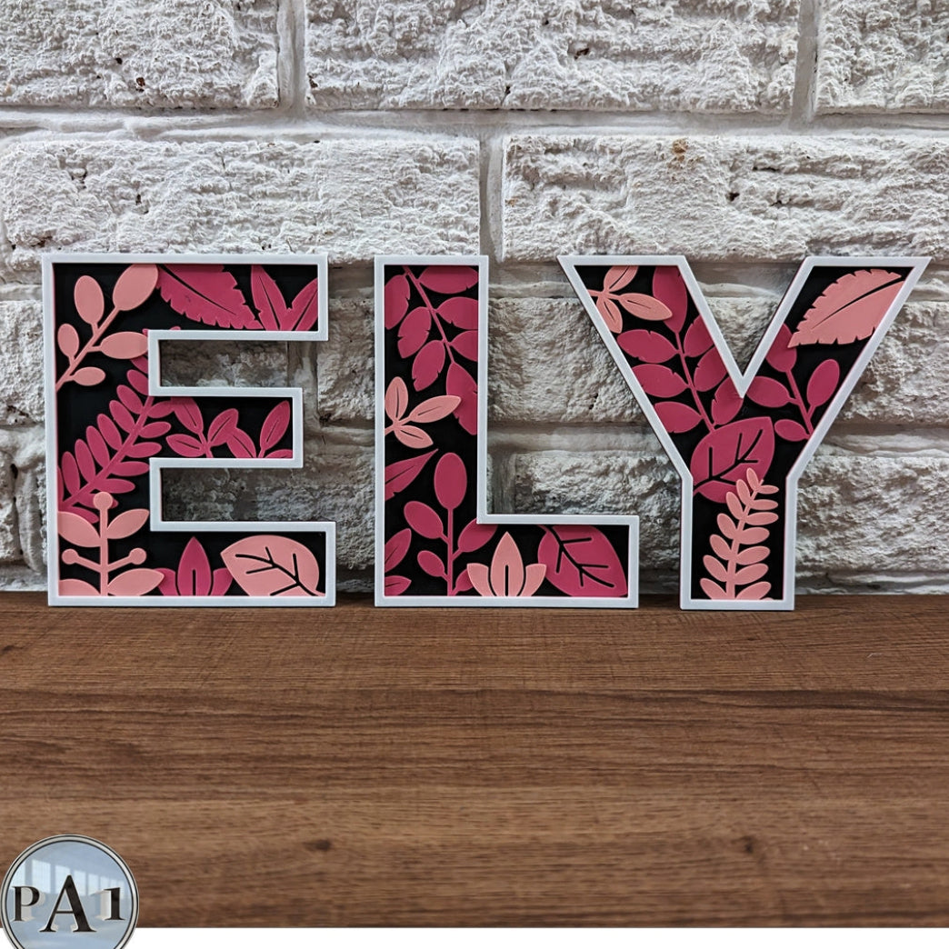 Decorative letters spelling 'ELY' with leaf pattern on a stone wall and wooden surface.