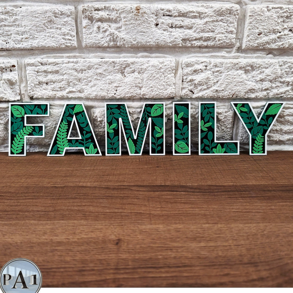 Decorative sign with 'FAMILY' in green leaf pattern on a wooden surface and brick wall background