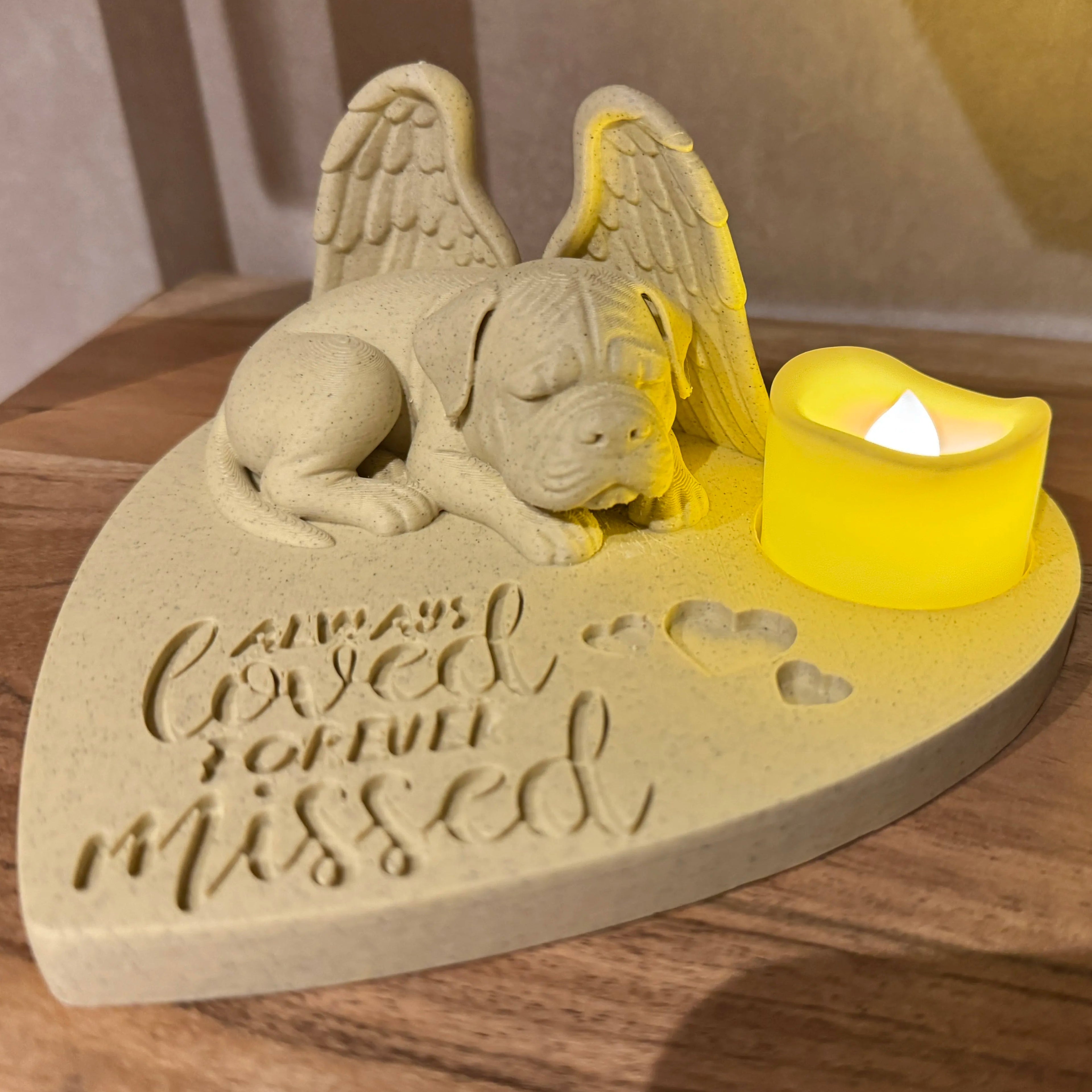 Memorial sculpture of a bullmastiff with angel wings and a candle on a heart-shaped base.