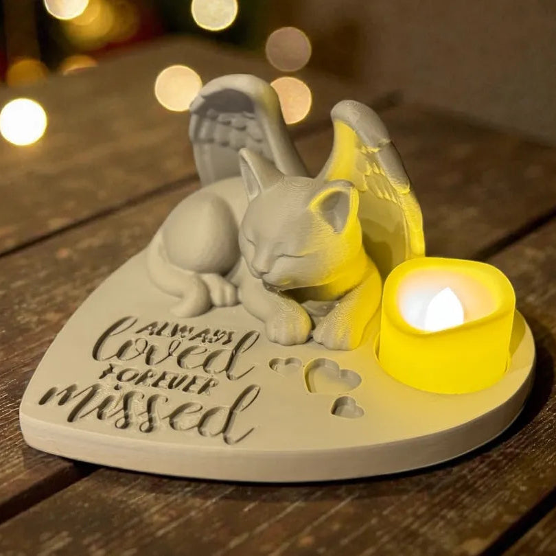 Memorial sculpture of a cat with a candle on a wooden surface, surrounded by blurred lights.
