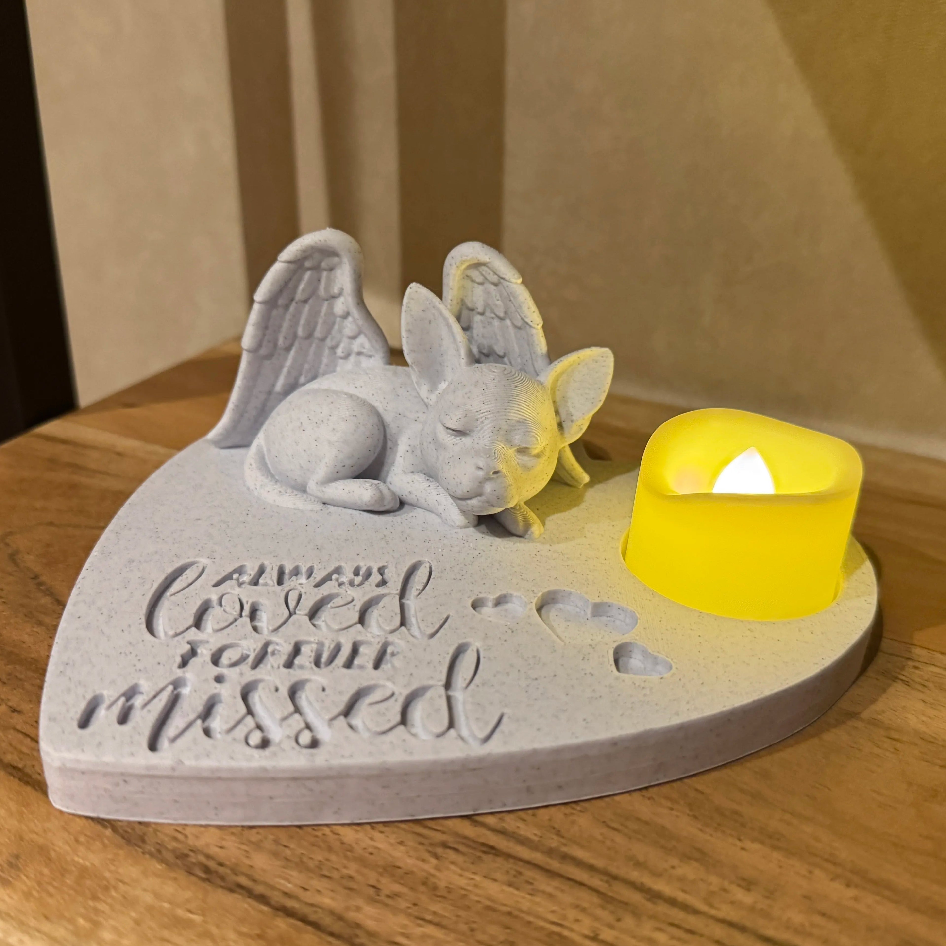 Memorial sculpture with angel wings and a candle on a wooden surface