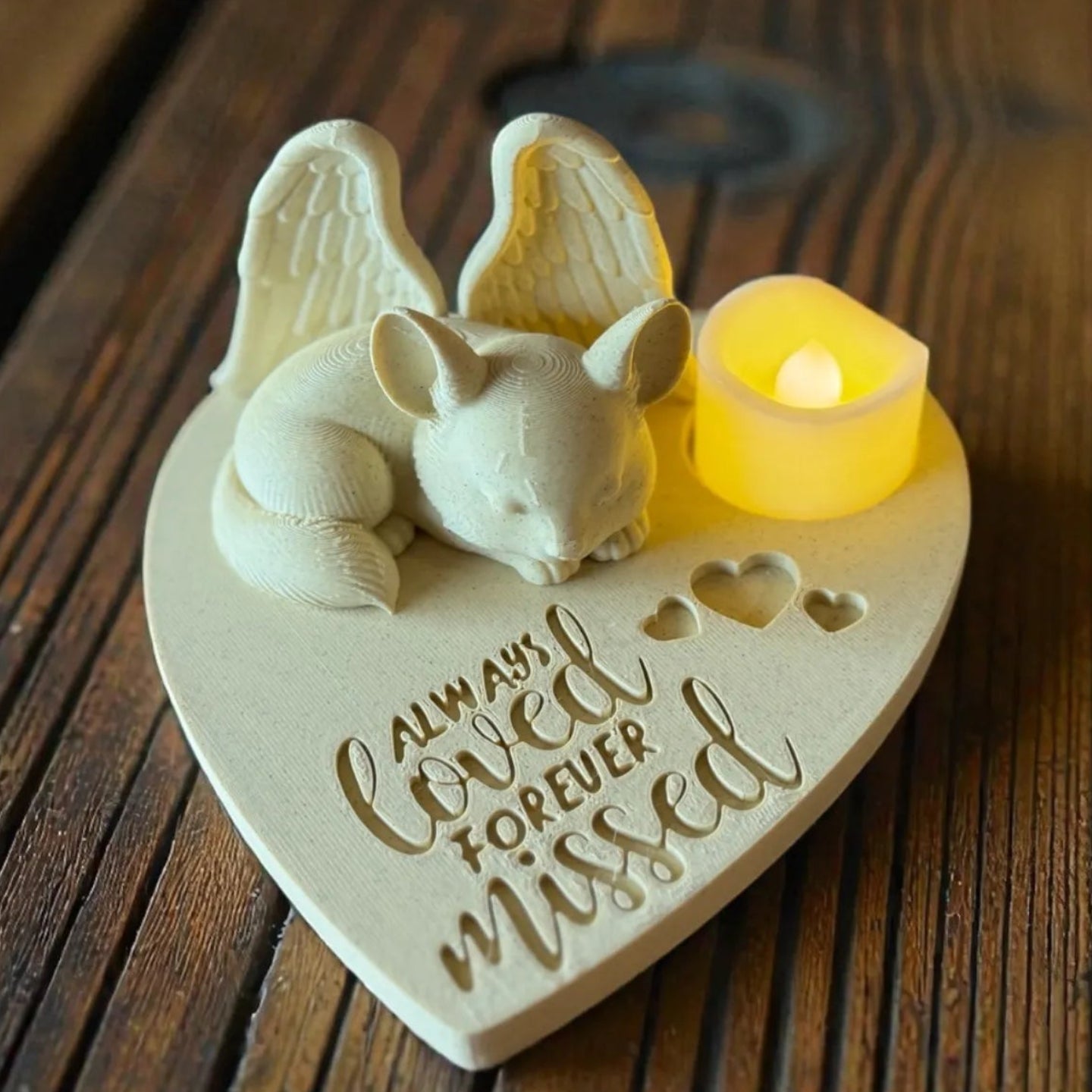 Heart-shaped memorial plaque with a small animal figurine and candle on a wooden surface