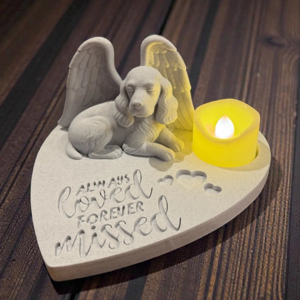 Memorial sculpture of a dog with angel wings and a candle on a wooden surface