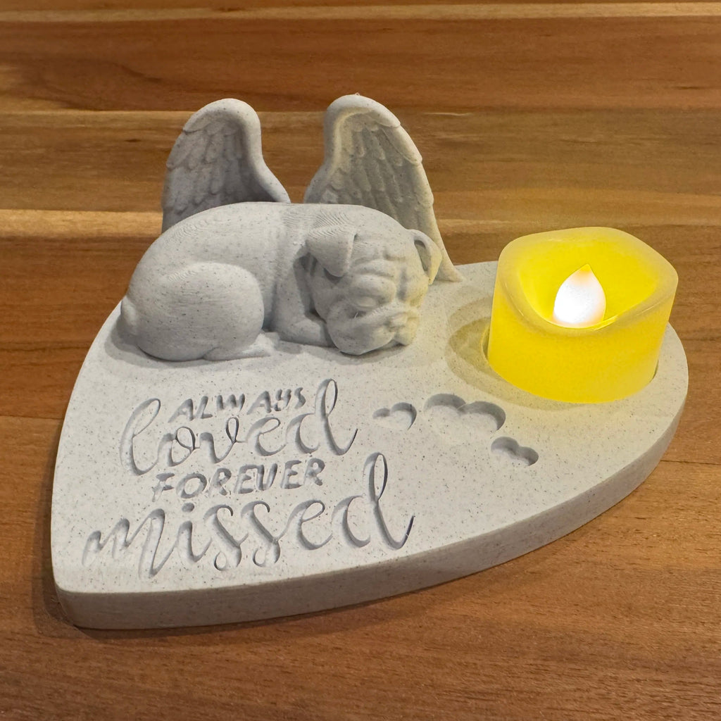 Memorial sculpture of a english bulldog with angel wings and a candle on a wooden surface