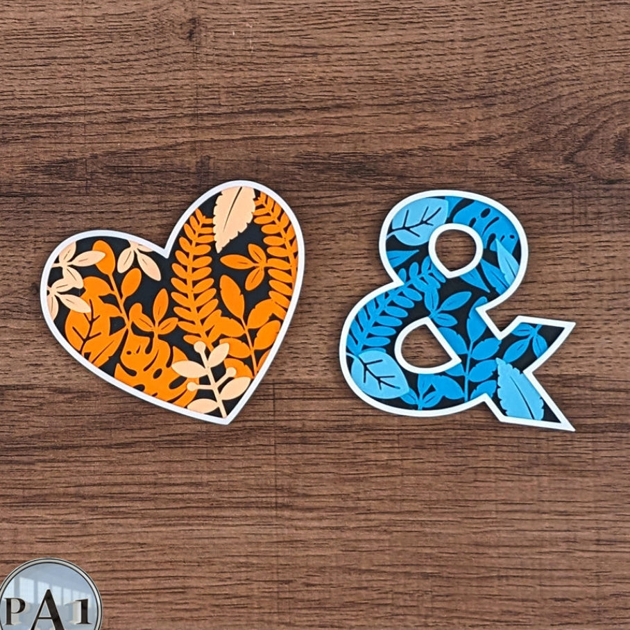 Heart-shaped and ampersand-shaped stickers with leaf patterns on a wooden surface