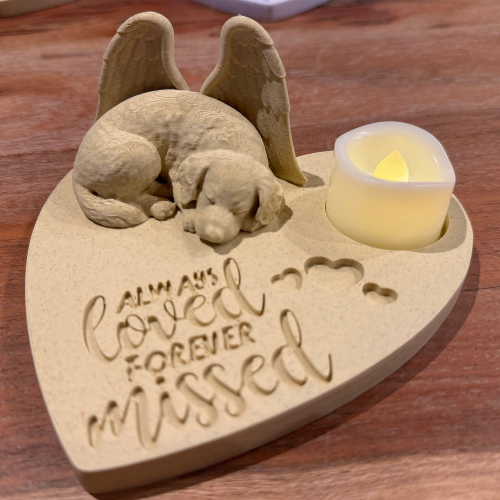 Heart-shaped memorial with golden retriever with Angel wings figurines and a candle on a wooden surface