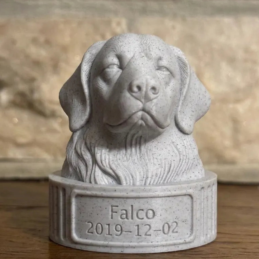 Gray stone sculpture of a Golden retriever's head, with 'Falco' and a date on a wooden surface