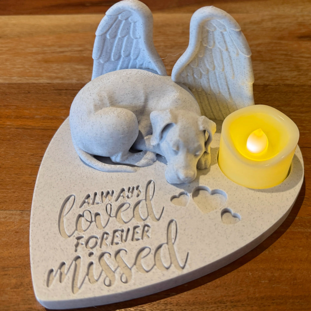 Memorial sculpture of a great dane with angel wings and a candle on a wooden surface