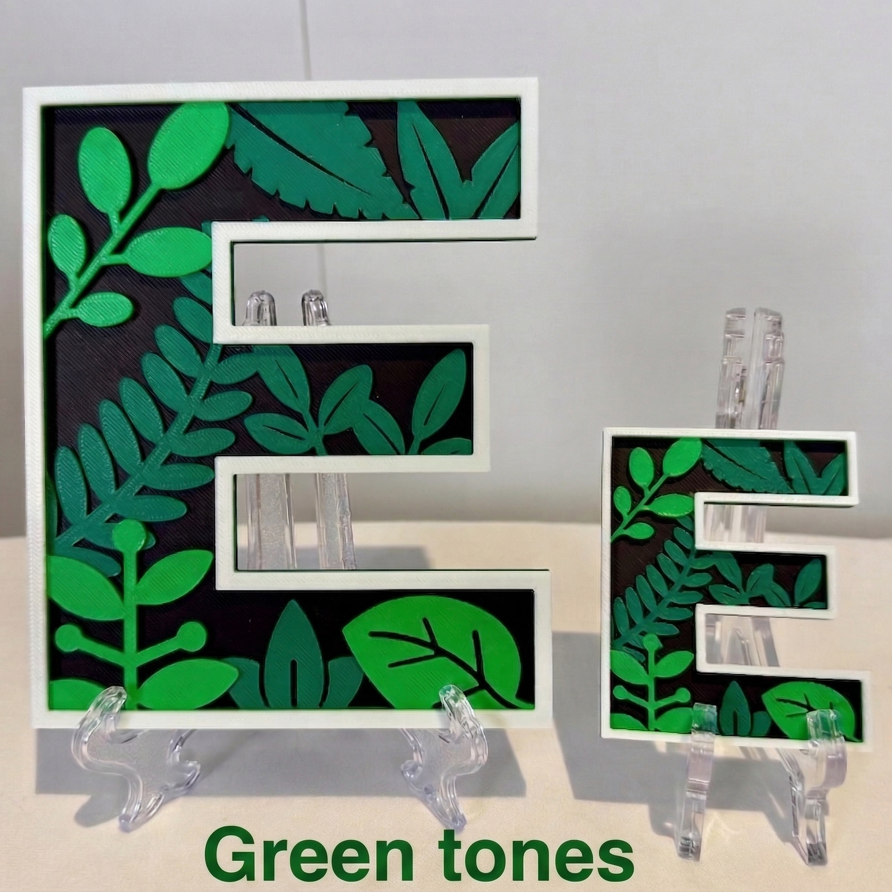Decorative letter 'E' with green leaf pattern on a stand against a neutral background