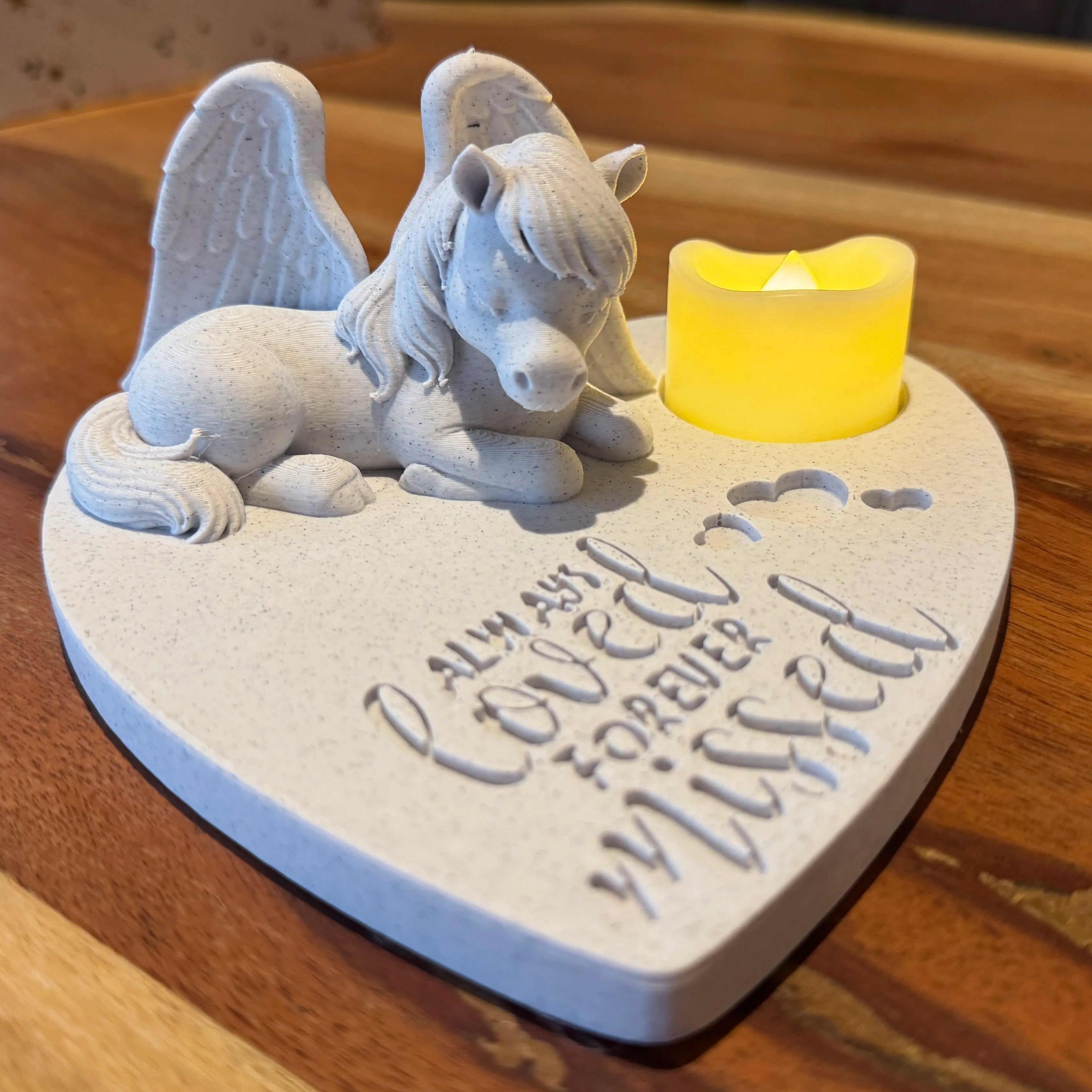 Decorative heart-shaped plaque featuring a horse with Angel wings figurine and lit candle on a wooden surface