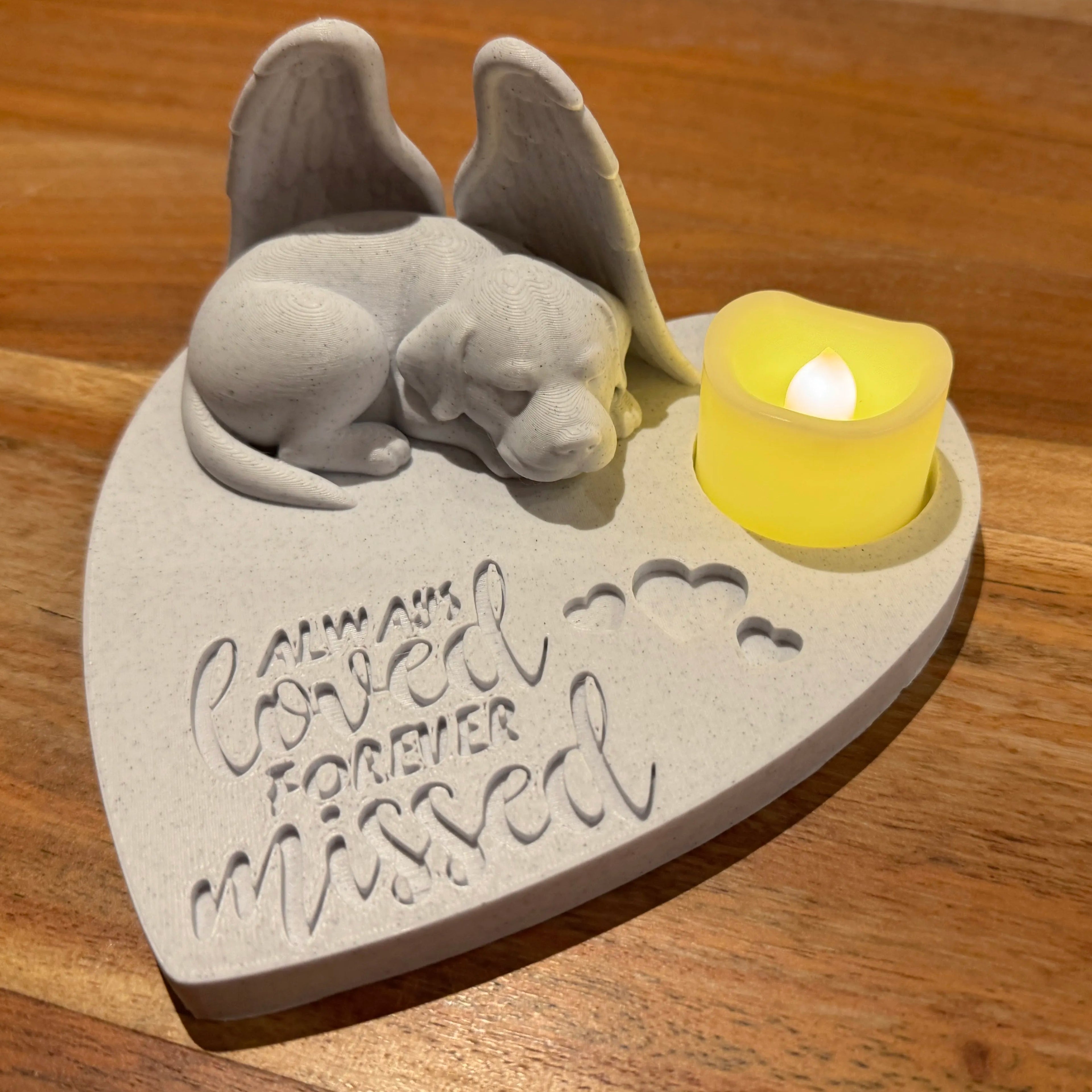 Memorial sculpture of a labrador retriever with Angel wings and a lit candle on a wooden surface