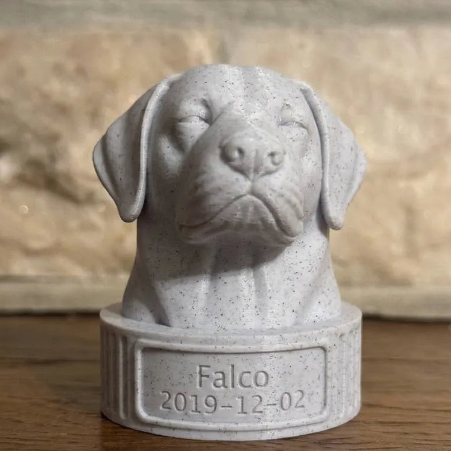 Gray stone sculpture of a labrador retriever dog's head with 'Falco' and a date engraved on a wooden surface.
