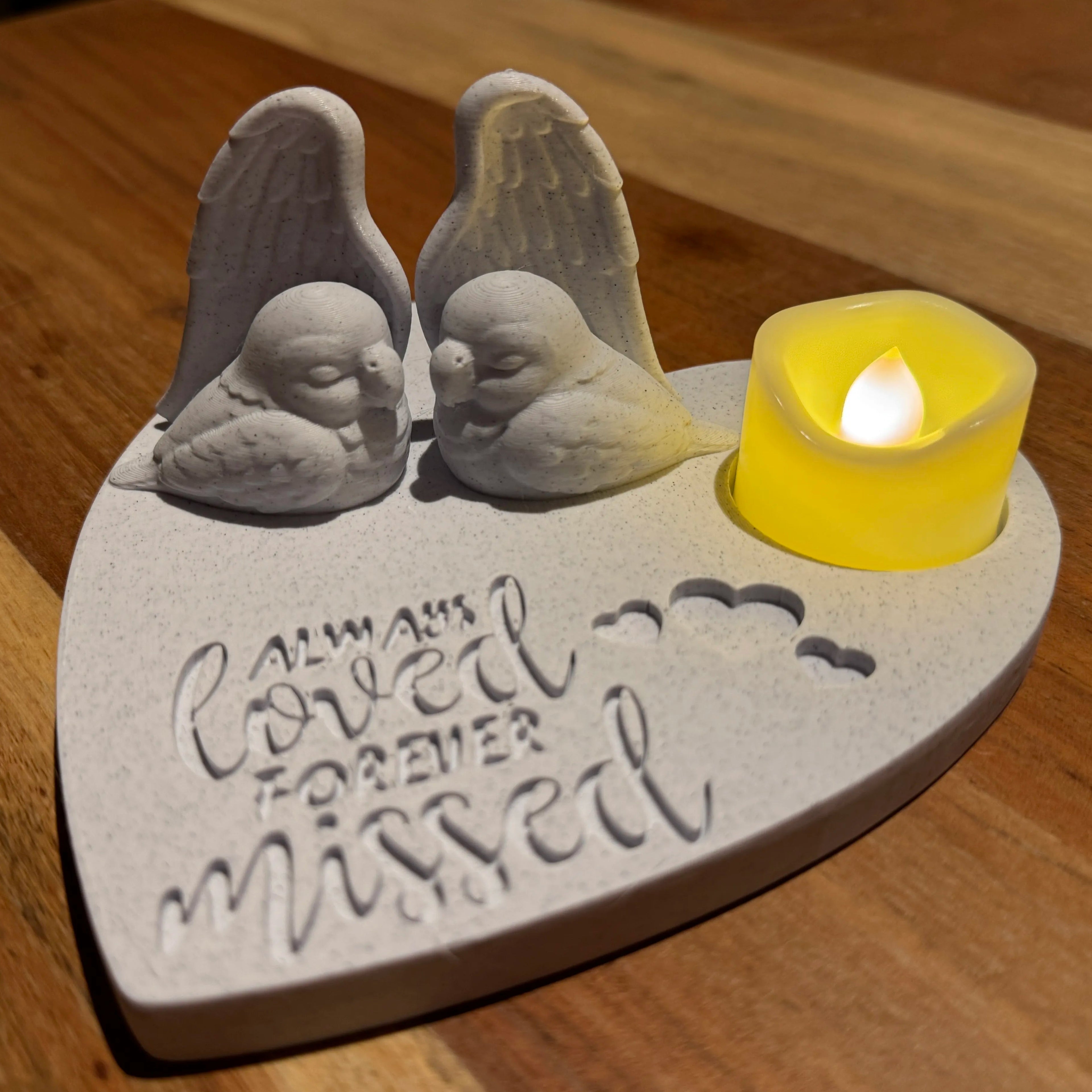 A heart shaped memorial featuring 2 lovebirds with Angel wings and a candle on a wooden surface