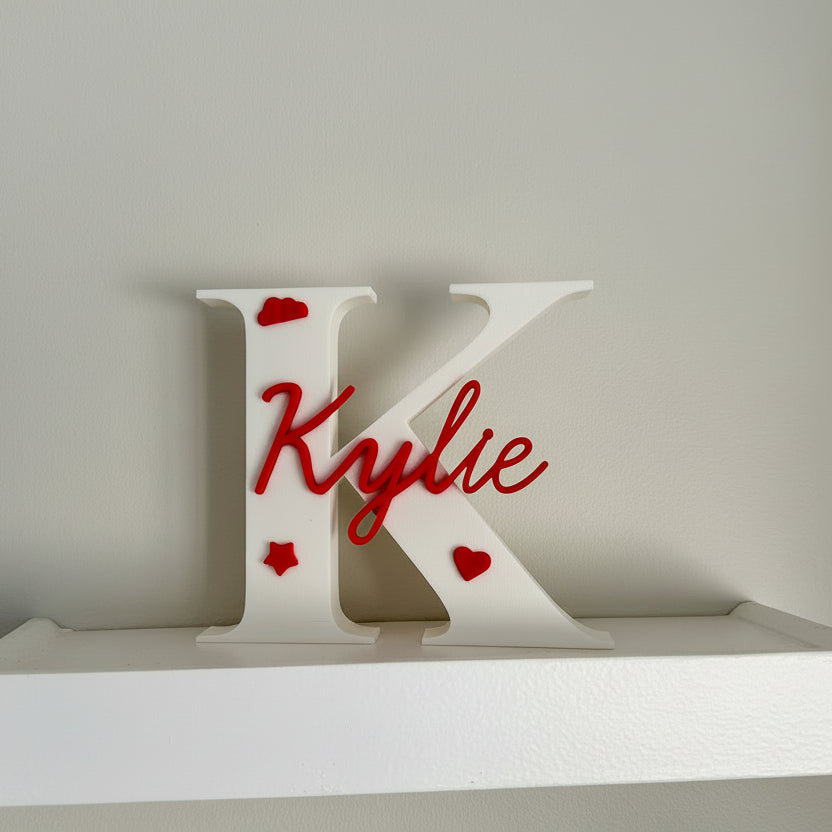 White letter 'K' with red text and hearts on a white platform against a gray background