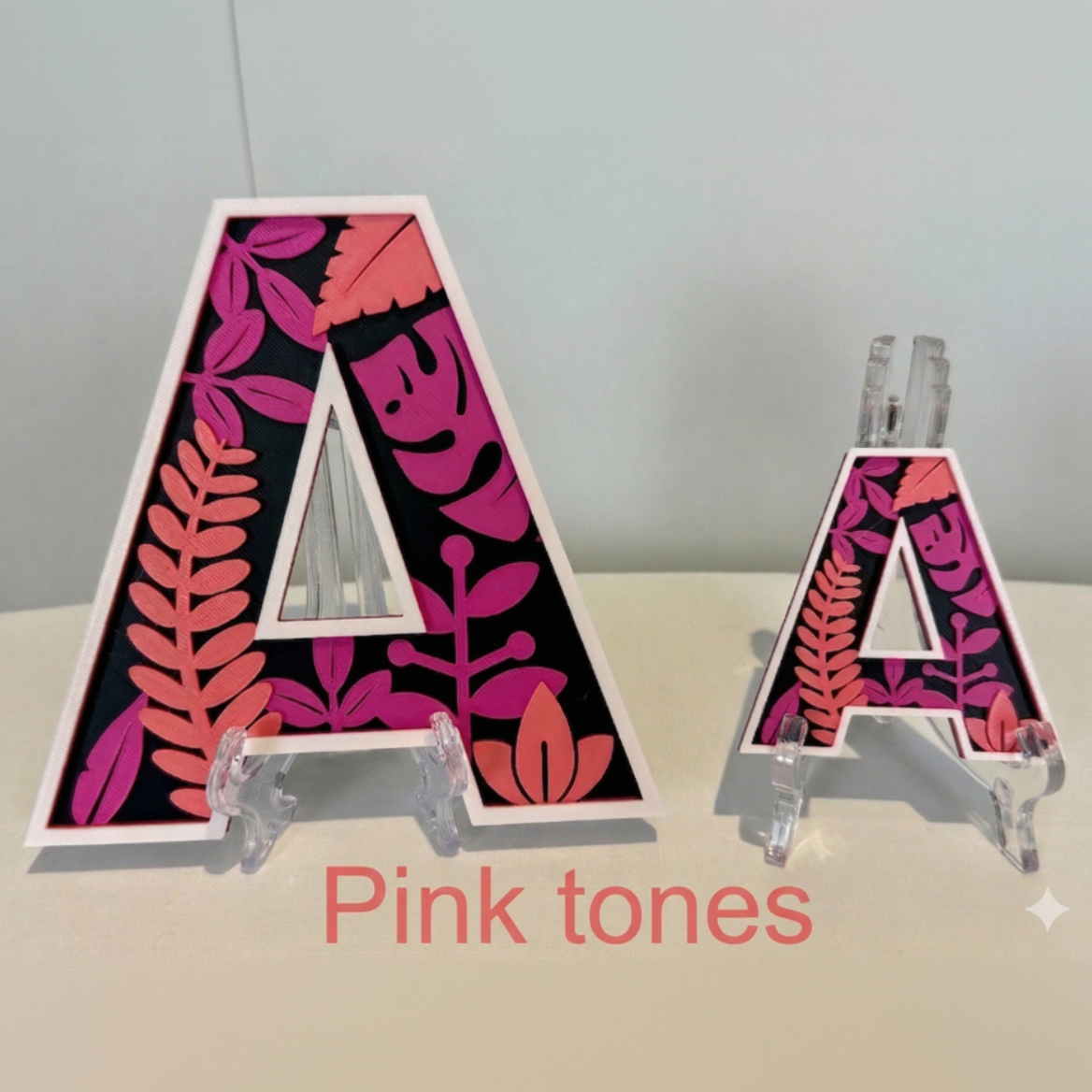 Floral-patterned letter 'A' with pink tones on a stand against a gray background.