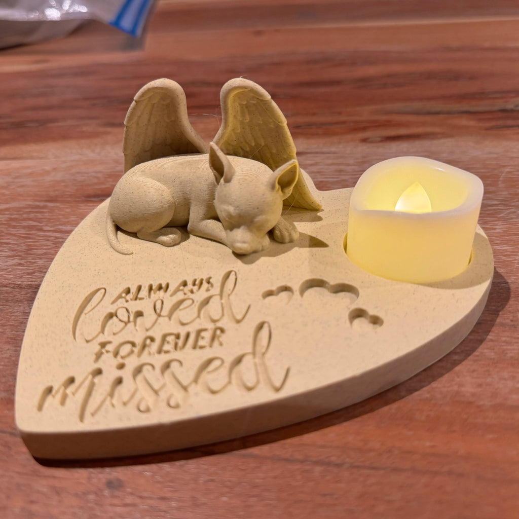 Heart-shaped wooden plaque with a pincer with wings figurine and a candle, engraved with 'Always loved forever missed', on a wooden surface.