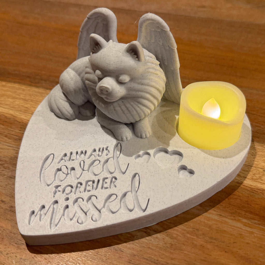 Heart-shaped pet memorial with a Pomeranian with Angel wings and a small candle on a wooden surface