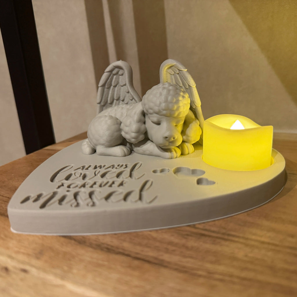 Decorative memorial featuring a poodle with Angel wings and a candle on a wooden surface