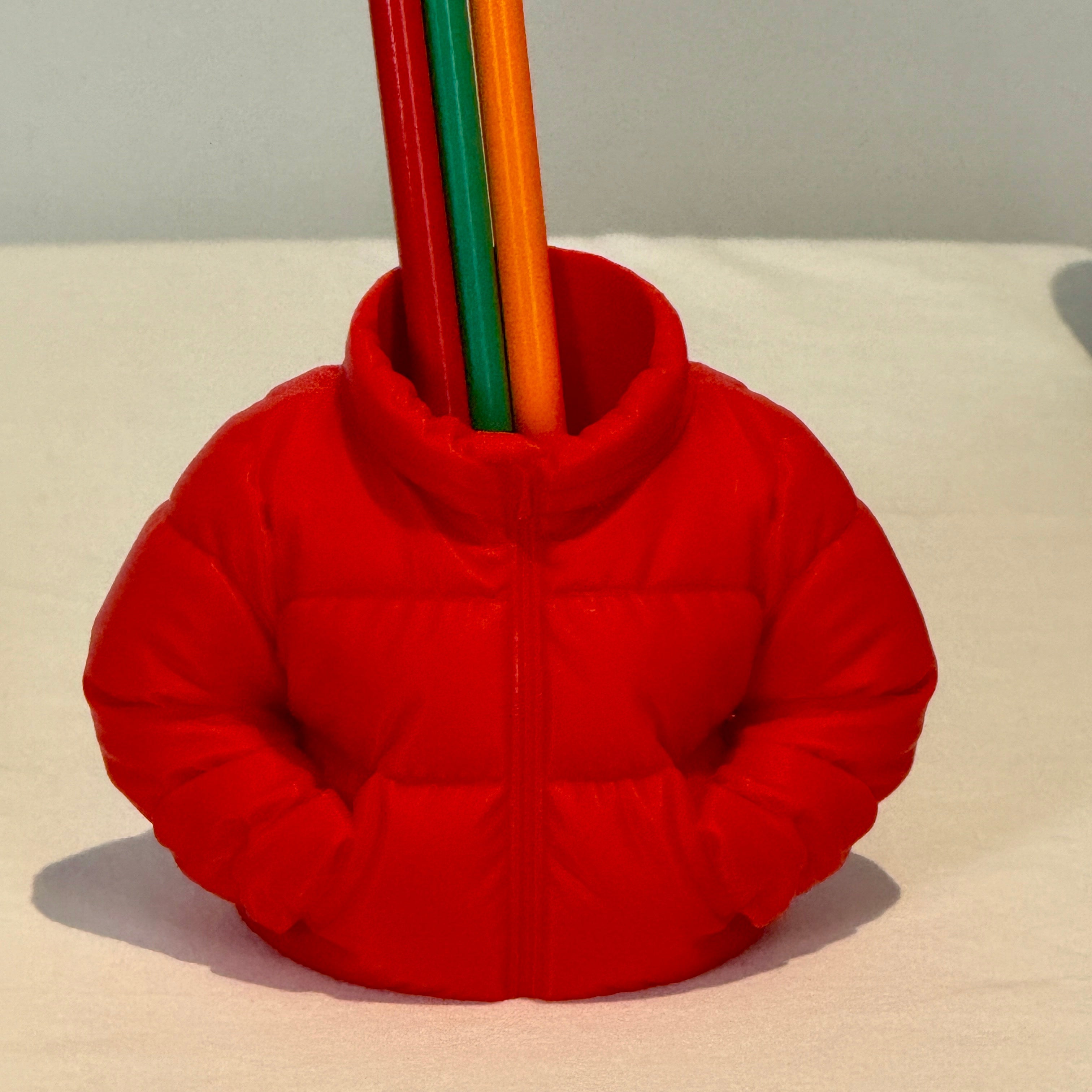 Red puffer jacket-shaped pencil holder with colorful pencils on a beige surface.