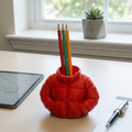 Red puffer jacket-shaped pen holder with colored pencils on a desk.