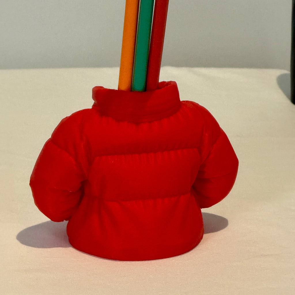 Red puffer jacket-shaped holder with colored pencils on a white background