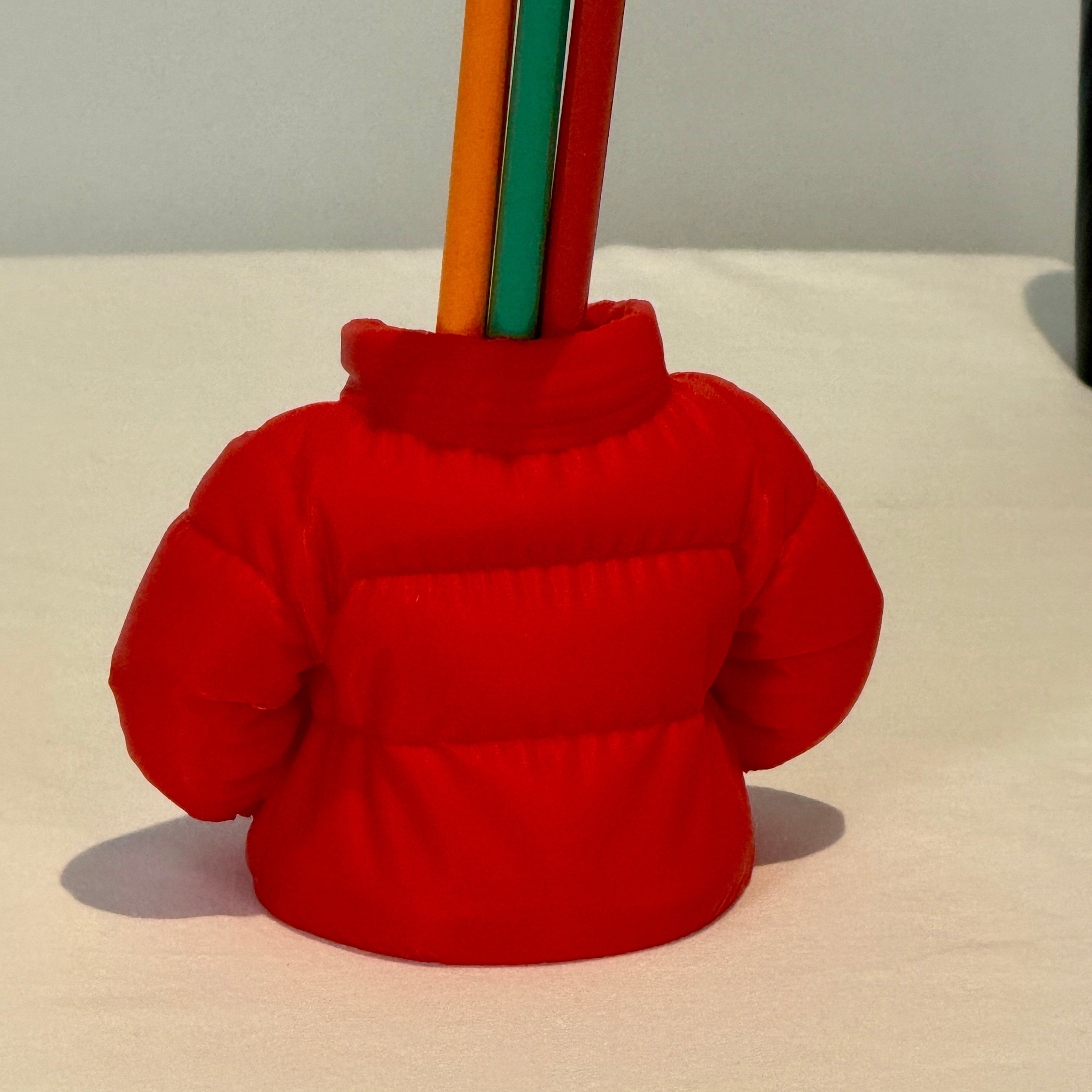 Red puffer jacket-shaped holder with colored pencils on a white background