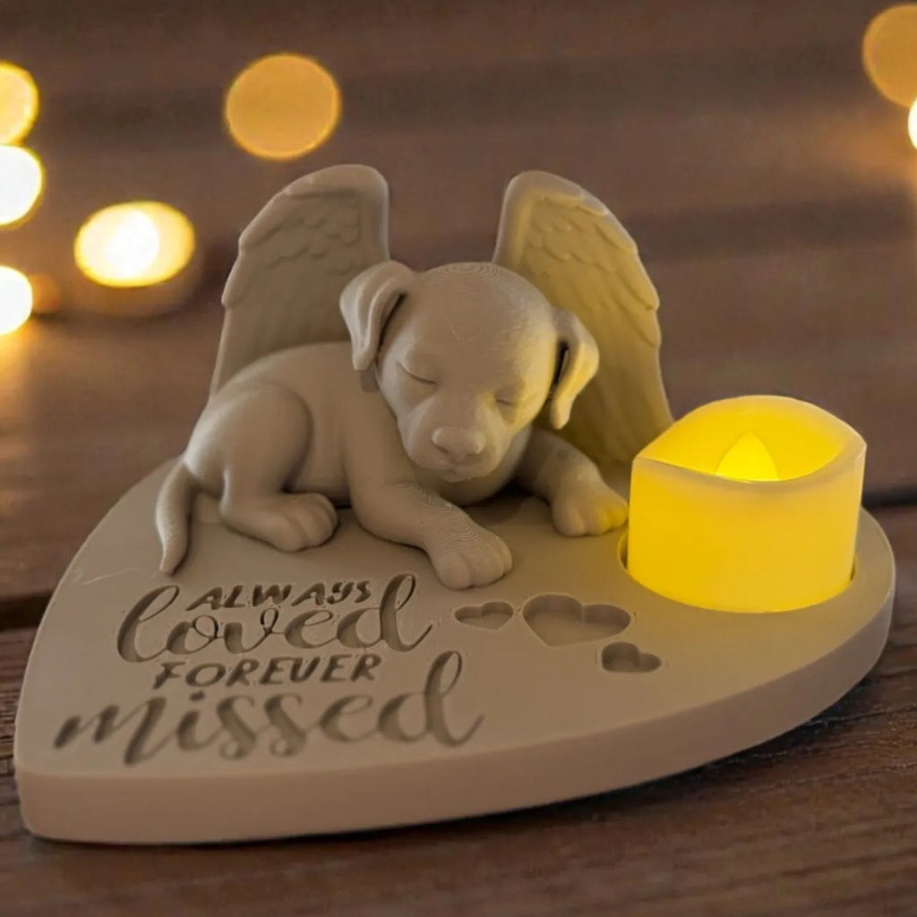 Memorial figurine of a puppy with angel wings and a candle on a wooden surface with blurred lights in the background.