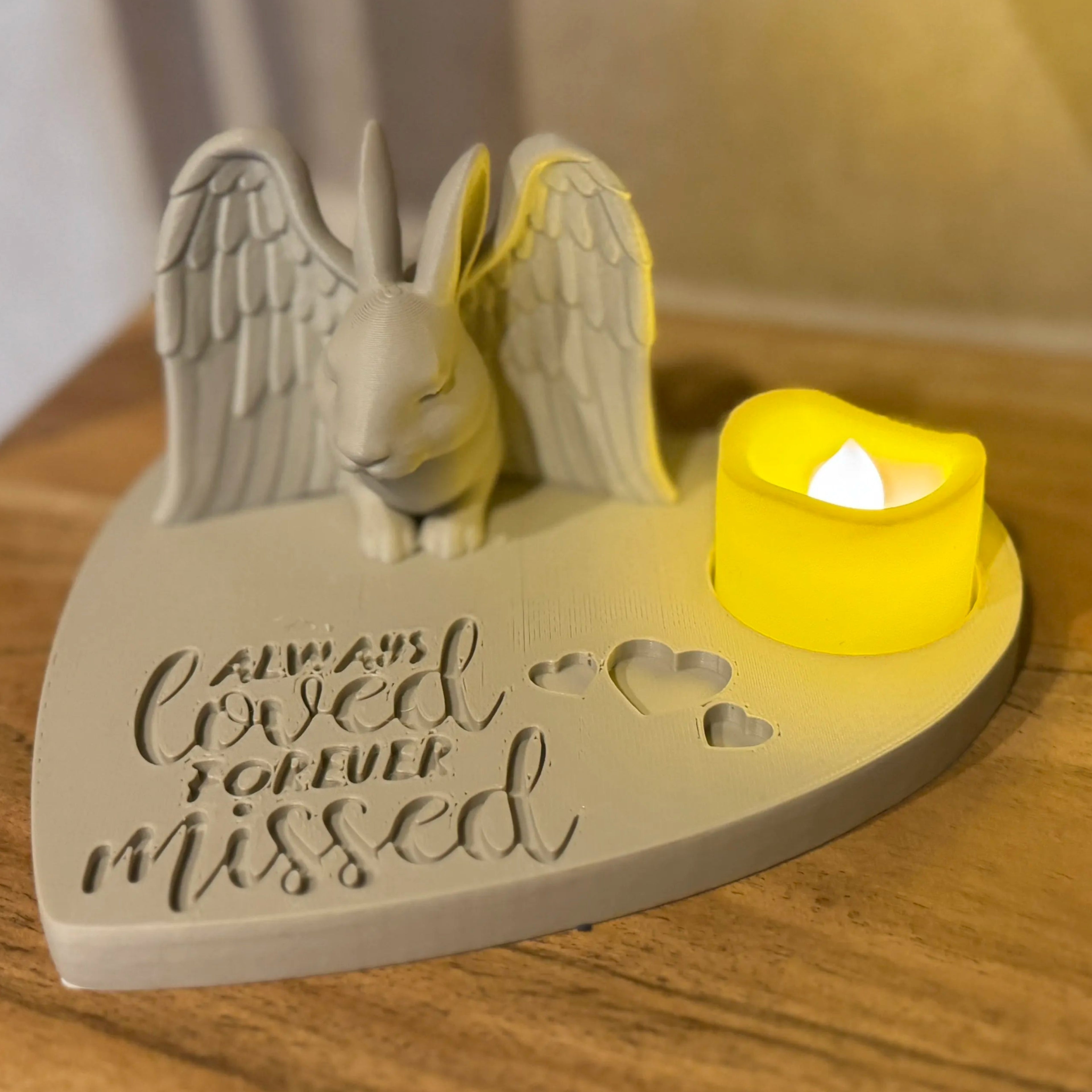 memorial featuring a rabbit with Angel wings figurine with a candle on a wooden surface