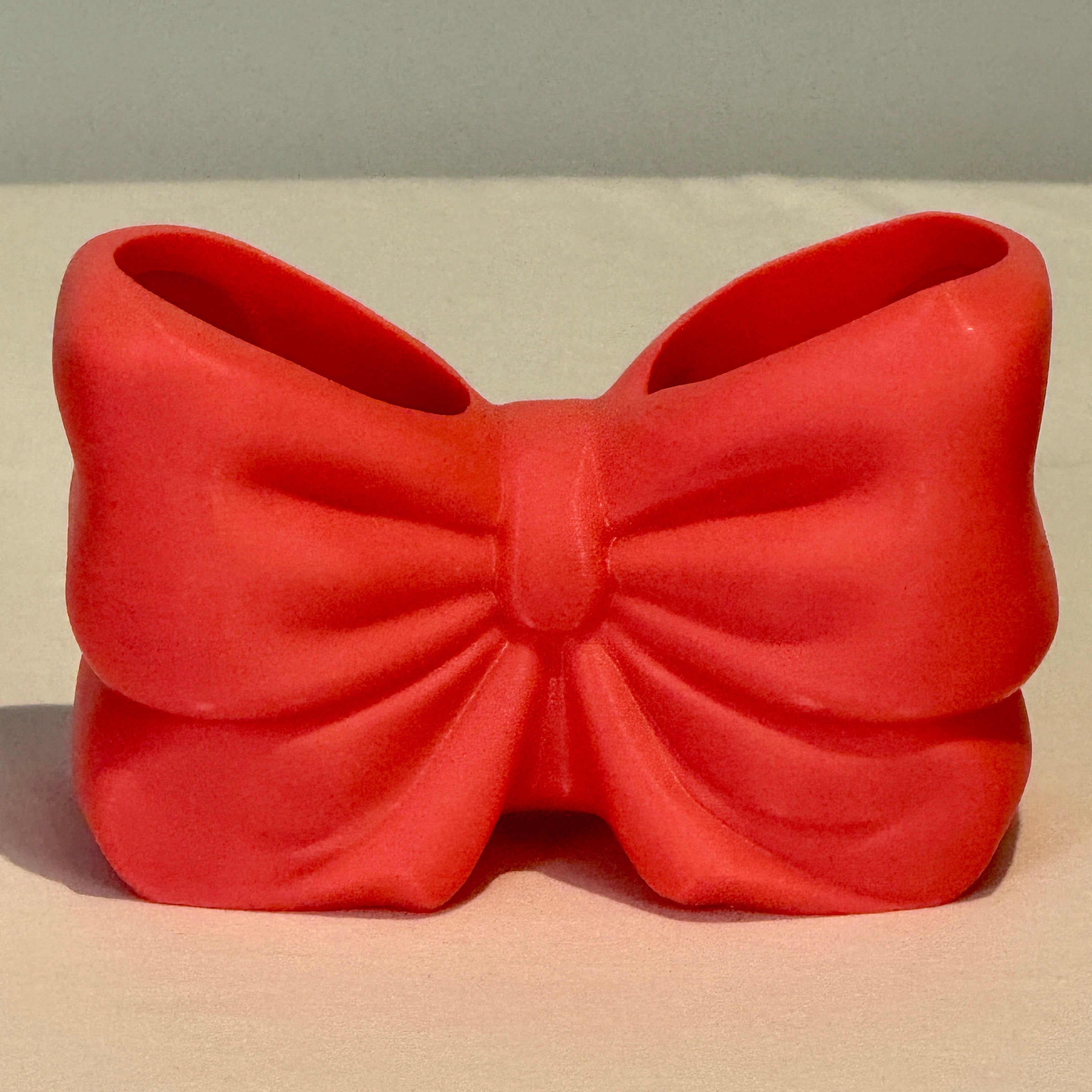 Red bow-shaped clutch on a beige surface with a light gray background