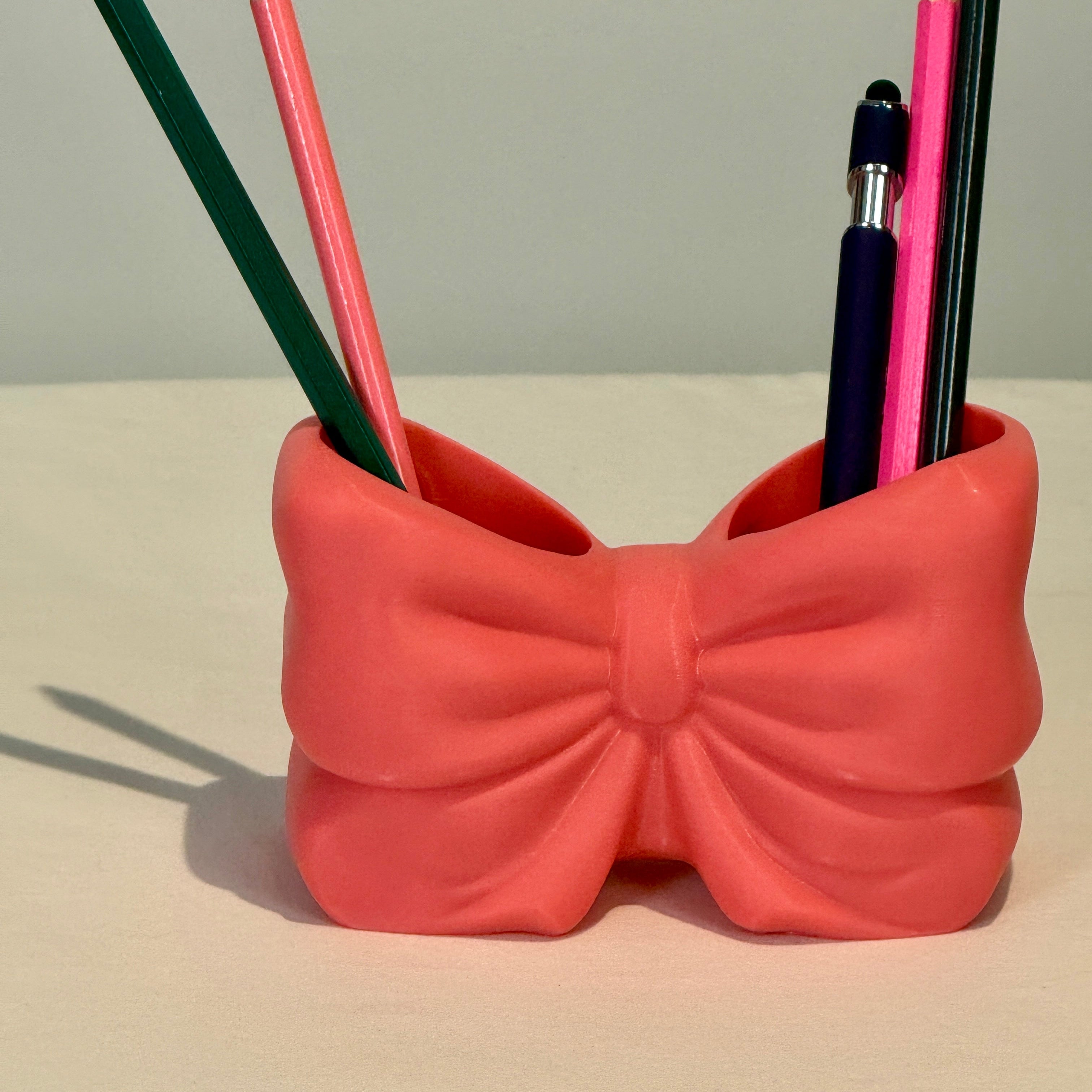 Pink bow-shaped pencil holder with pencils on a light background