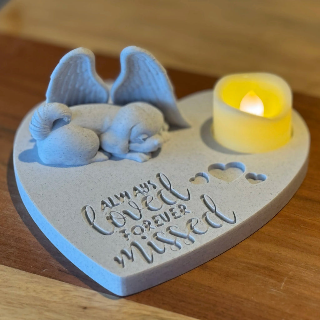 Heart-shaped memorial of a Shih tzu with angel wings figurine and candle on a wooden surface