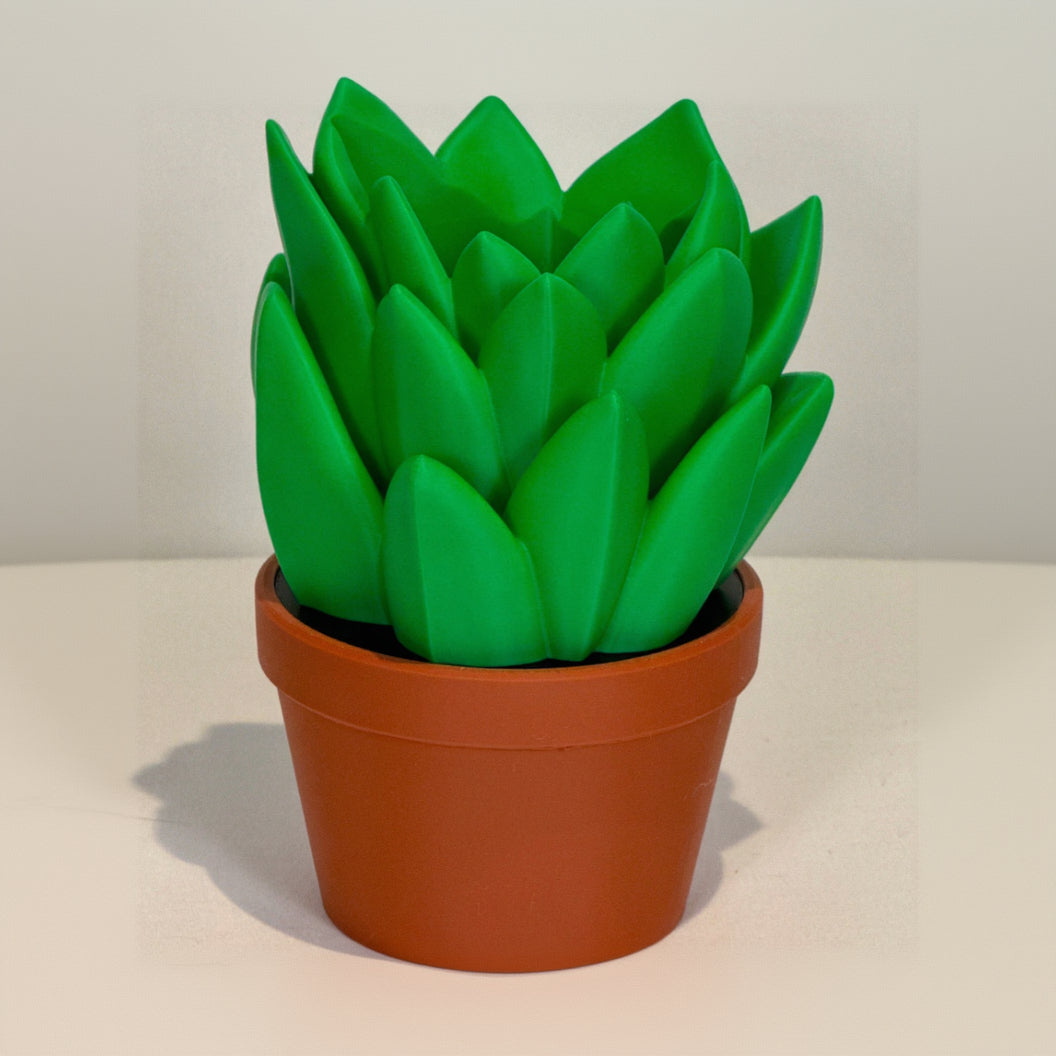 Green artificial plant in a terracotta pot on a white surface with a light gray background